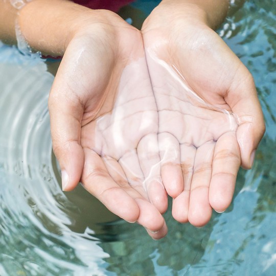 Hände schöpfen Wasser aus einer Quelle 