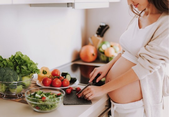 Schwangere Frau bereitet in der Küche einen Salat zu. 